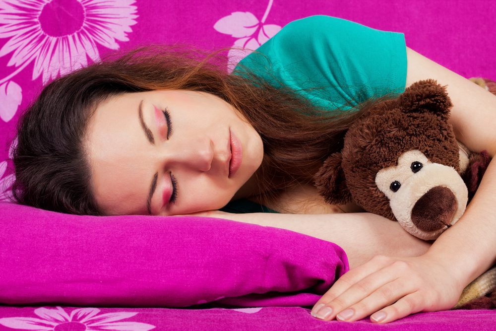young lady sleeping on bright pink sheets with brown teddy bear